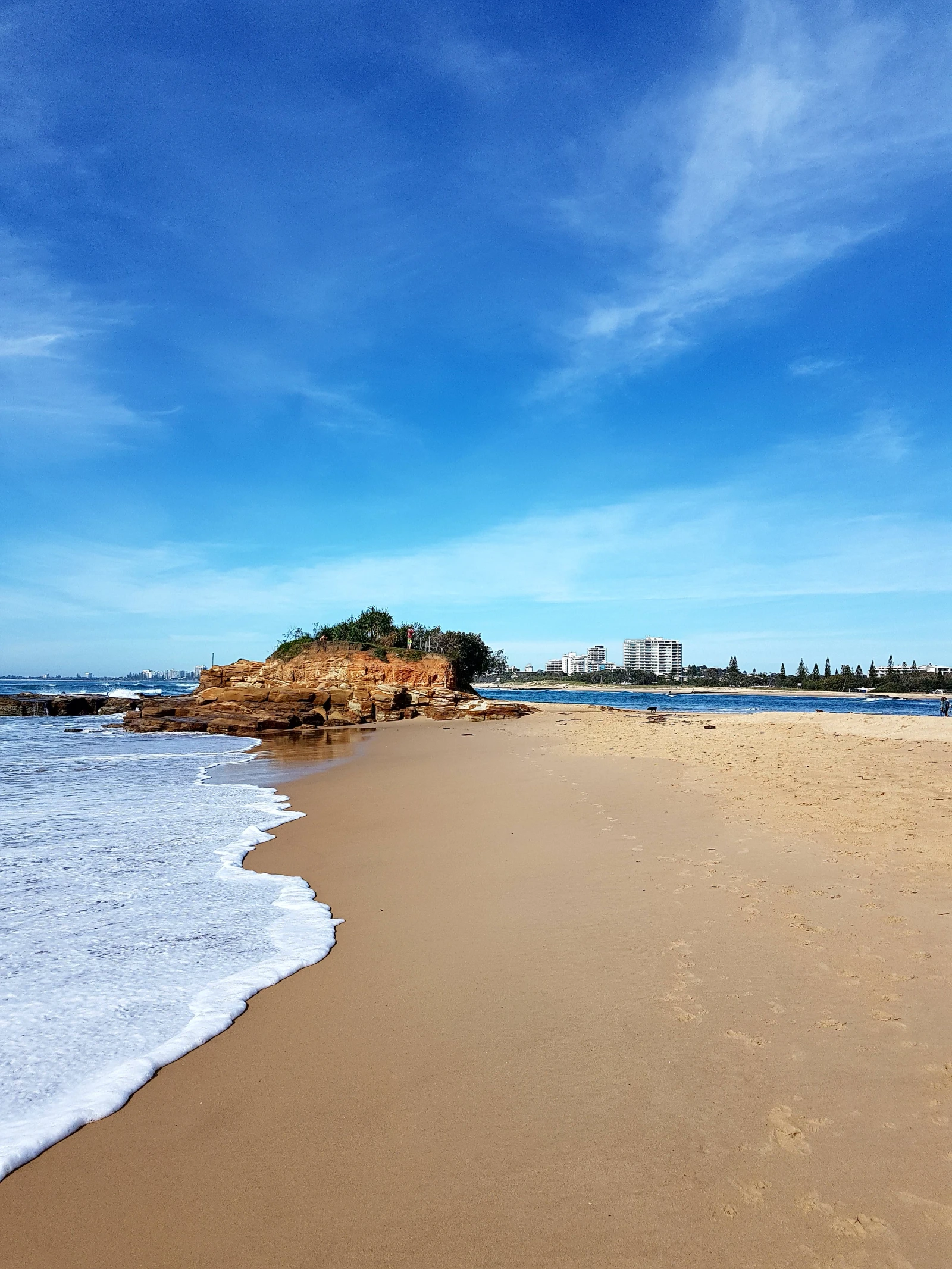Sunshine Coast beach with surf, a rocky outcrop and coastal buildings